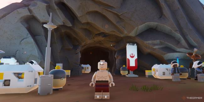 A screenshot from Lego Fortnite showing the player as Avatar Aang standing outside a cave that has Lego Star Wars gear around and a rebel insignia on a banner near the entrance.